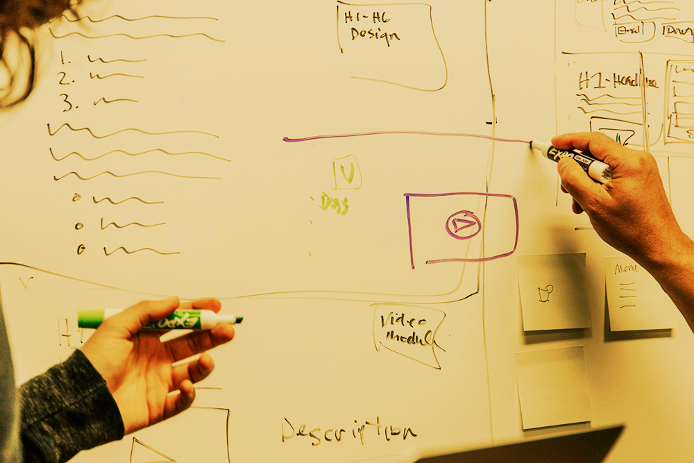 Overlapping handwritten project roles and arrows on a whiteboard, representing blurred responsibilities